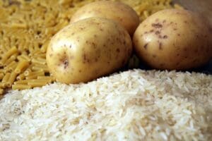 Rice, potatoes and macaroni pasta on a wooden table.Three common carbohydrates which provide energy but can cause obesity