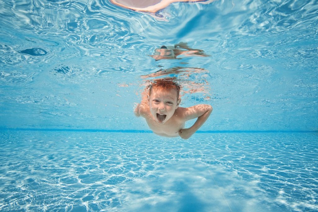 Happy young boy swim and dive underwater, kid breast